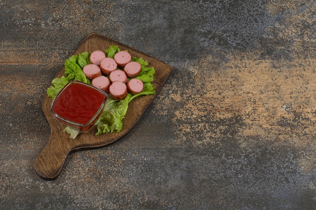 Fried sliced sausages and ketchup on wooden board.