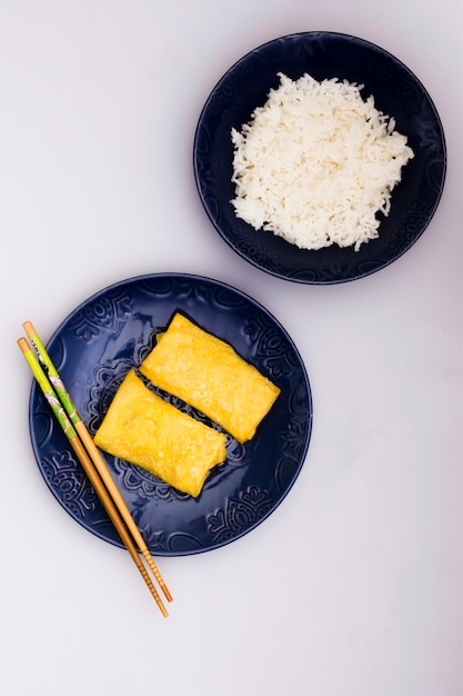 白い背景の上の平野ご飯の近くのお箸で皿に揚げ春巻き