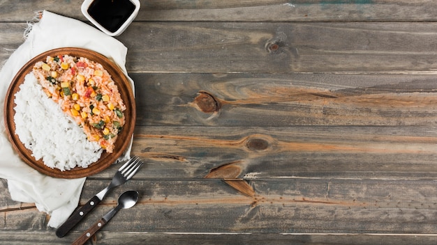 Fried and steamed rice on wooden plate with fork and spoon over the table