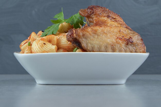 Fried wings and seashell pasta in white bowl.