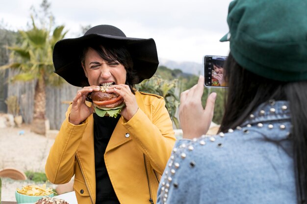 ハンバーガーを食べる女性の写真を撮る友人