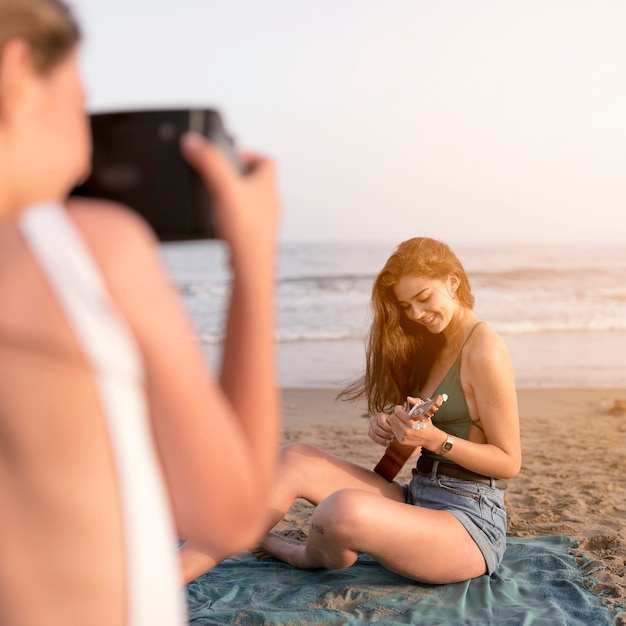 무료 사진 해변에서 우쿨렐레를 연주하는 여자의 selfie를 복용하는 친구