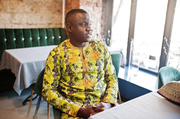 Дружелюбный афро-мужчина в традиционной желтой одежде сидит в ресторане