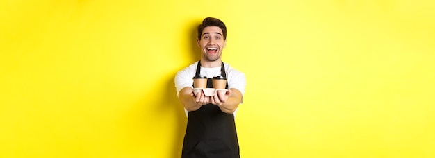 Foto gratuita barista amichevole in grembiule nero che dà l'ordine da asporto tenendo due tazze di caffè e sorridendo in piedi