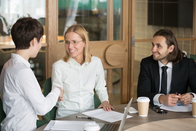 Friendly businesswomen shaking hands at group office meeting with businessman