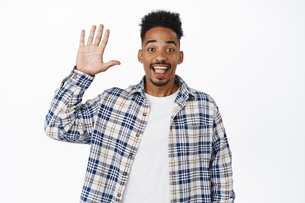 Foto gratuita amichevole e allegro uomo afroamericano agitando la mano, sorridendo felice e salutando, salutando, salutandoti gesto, accogliendo le persone, in piedi su sfondo bianco