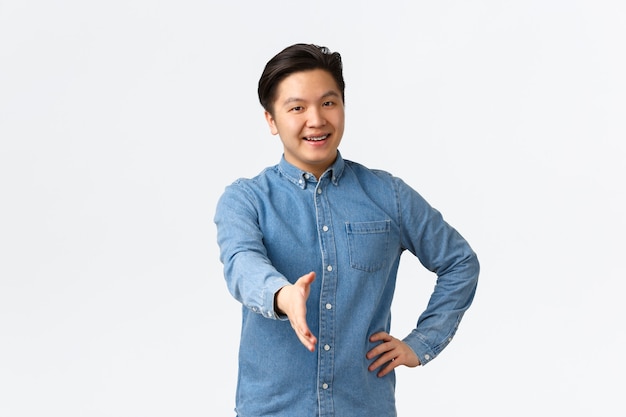 Friendly cheerful asian man searching for job, come to interview, extending hand for handshake, greeting someone, welcome to office, saying hello with happy smile, white background