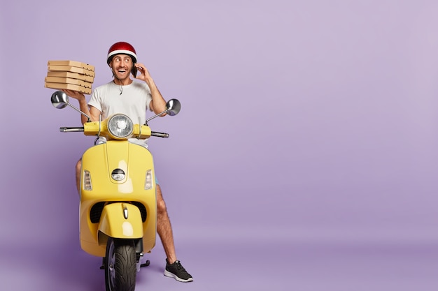 Free photo friendly deliveryman driving scooter while holding pizza boxes