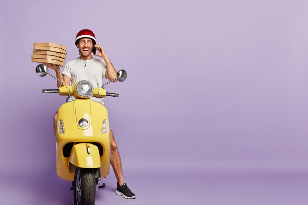 Friendly deliveryman driving scooter while holding pizza boxes