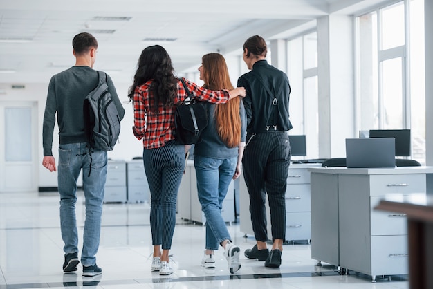 Friendly embracings. Group of young people walking in the office at their break time