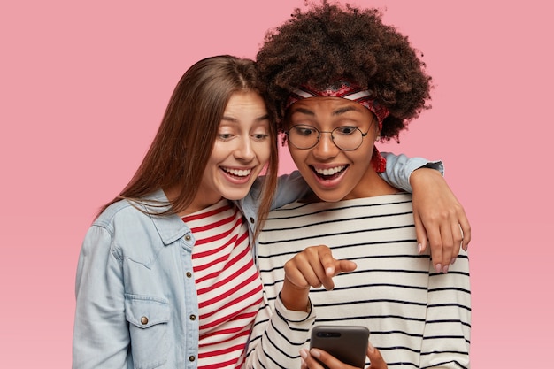 Amiche amiche si divertono insieme, si abbracciano e guardano video divertenti sul cellulare