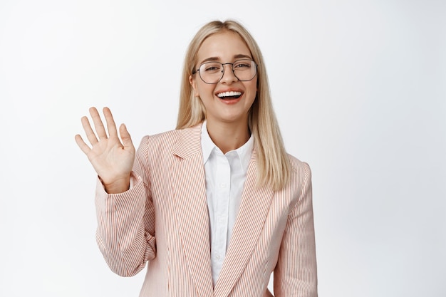 Friendly female office worker waving hand saying hello greeting and smiling standing over white background