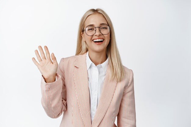 Friendly female office worker waving hand saying hello greeting and smiling standing over white background