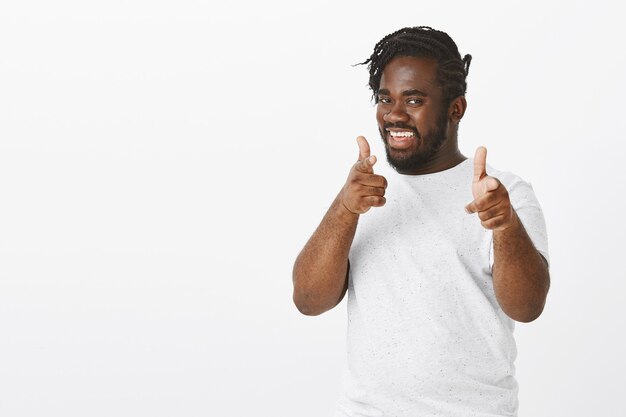 Friendly good-looking guy with braids posing against the white wall