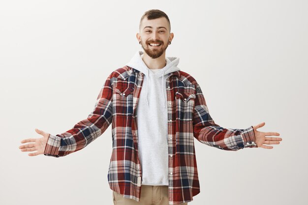 Friendly happy hipster spread hands sideways and greet people, smiling surprised