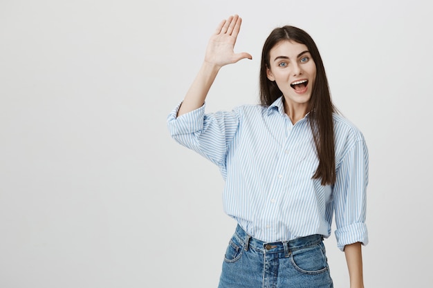 Friendly happy pretty woman waving raised hand in hello, greeting gesture