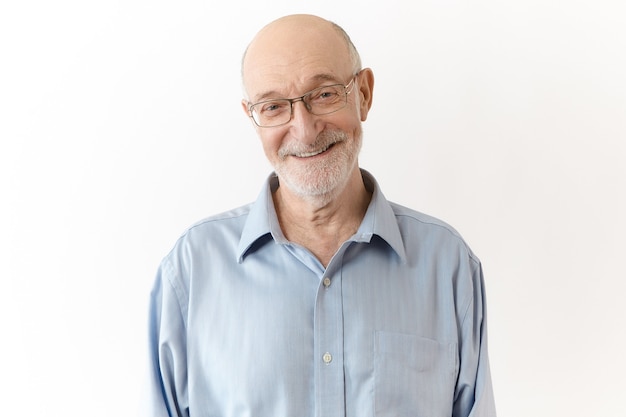 Friendly humorous grandpa with white beard smiling joyfully at camera. Elegant neat elderly businessman in glasses, rejoicing at successful effective work results, posing isolated in studio