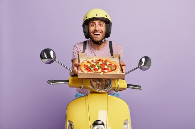 Friendly looking deliveryman driving yellow scooter while holding pizza box