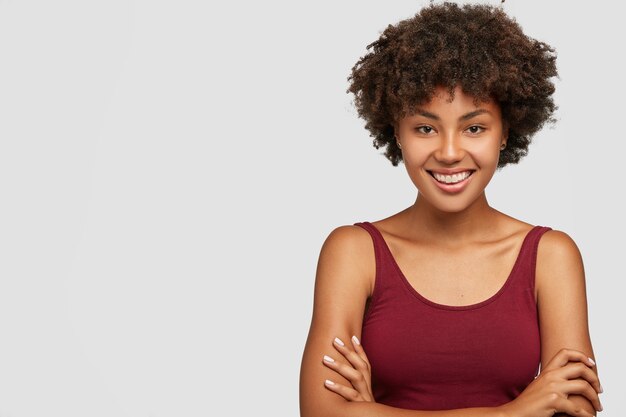 Friendly looking self assured dark skinned young girl keeps arms folded