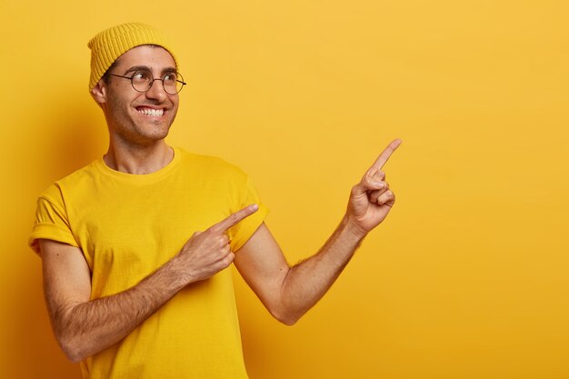 Friendly looking smiling man customer advertises sale on copy space right, points index fingers, recommends going this direction