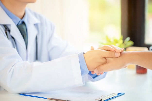 Friendly man doctor's hands holding male patient's hand for encouragement and empathy. 