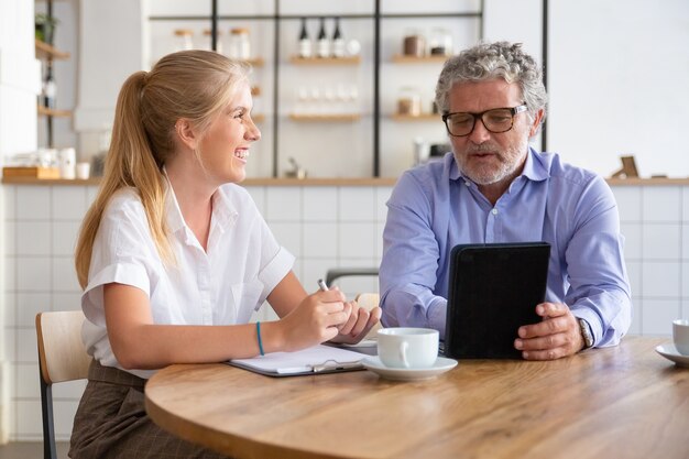 Friendly mature mentor explaining project detail to joyful intern