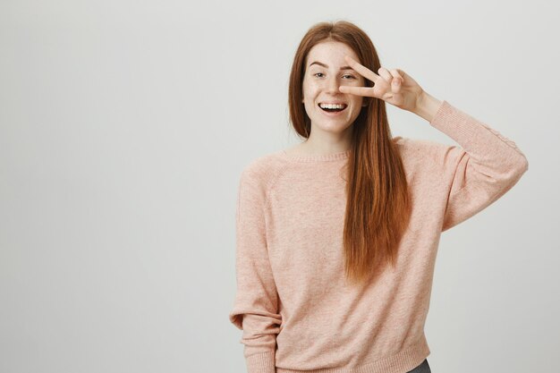 Friendly optimistic redhead girl smiling and showing peace sign
