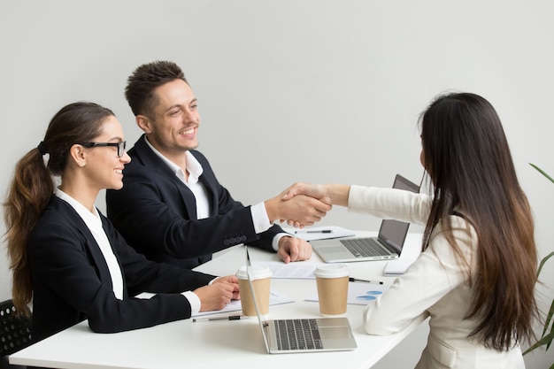 Friendly partners handshaking at group meeting thanking for successful teamwork