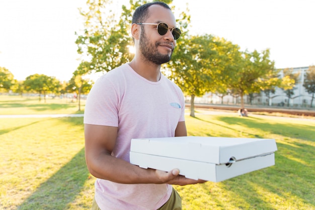 Ragazzo bello positivo amichevole che trasportano pizza