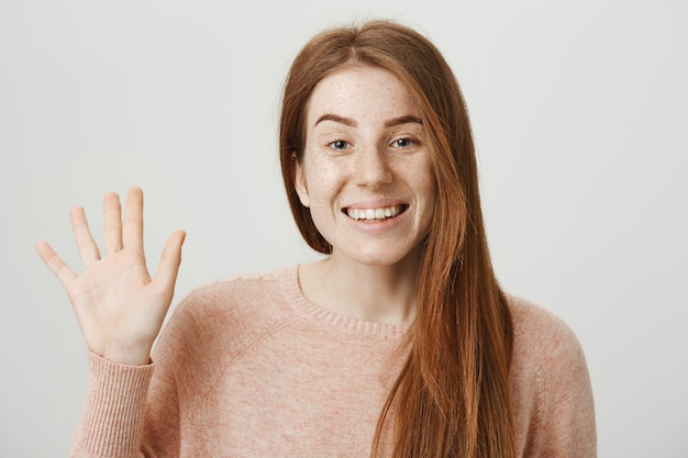 Amichevole ragazza rossa agitando la mano per dire ciao, saluto