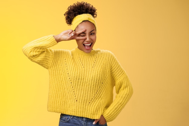 Friendly self-assured energetic african-american smiling healthy girl winking positive attitude grinning cheerful show peace victory lucky gesture hold hand waist confident, yellow background.