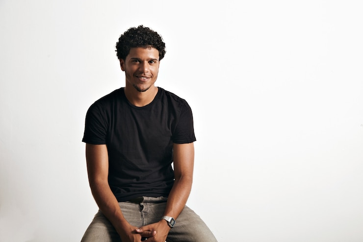 Free Photo friendly smiling young man in unlabeled cotton black t-shirt and jeans sitting on chair isolated on white