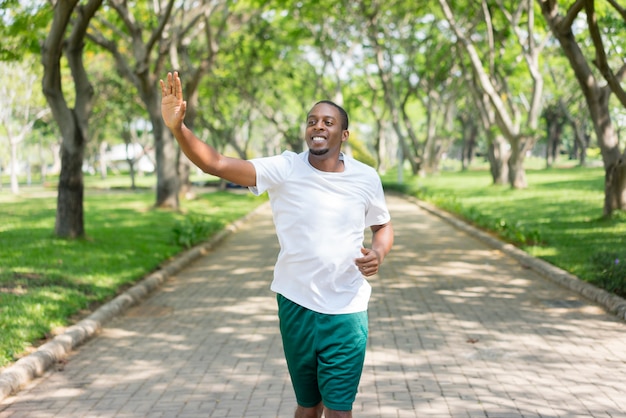 Friendly sporty black guy jogging in city park and greeting familiar sportsmen.