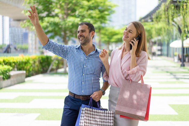 Friendly stylish couple of shoppers greeting someone on street.