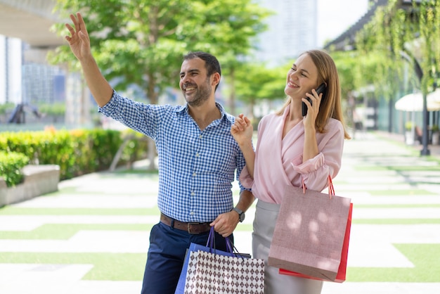 Friendly stylish couple of shoppers greeting someone on street.