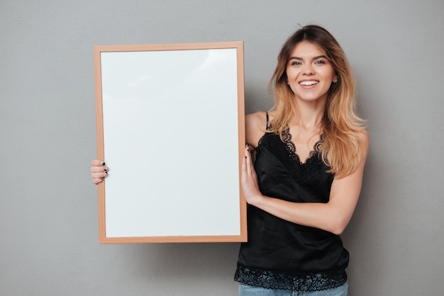 friendly woman holding blank board and looking at camera