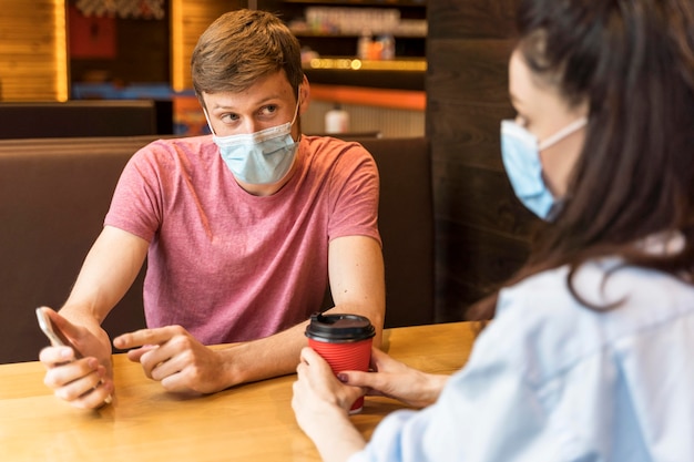 Free photo friends chatting while wearing medical masks indoors