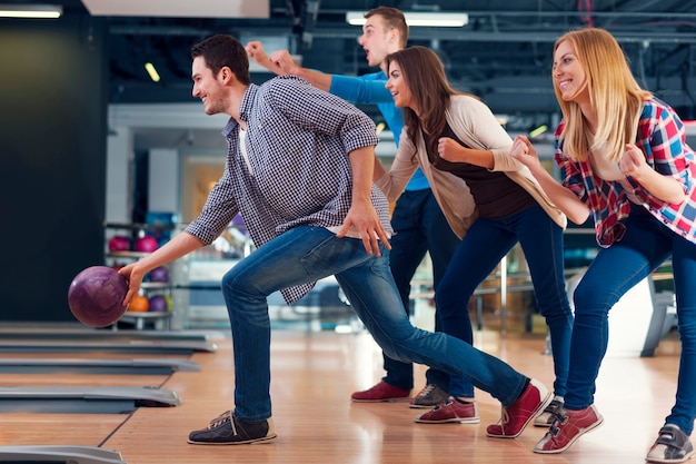 Foto gratuita amici che incoraggiano il loro amico mentre lanciano la palla da bowling