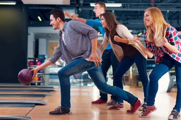 Friends cheering their friend while throwing bowling ball 

