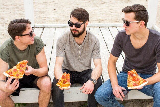 Friends conversing while sitting with pizza on beach