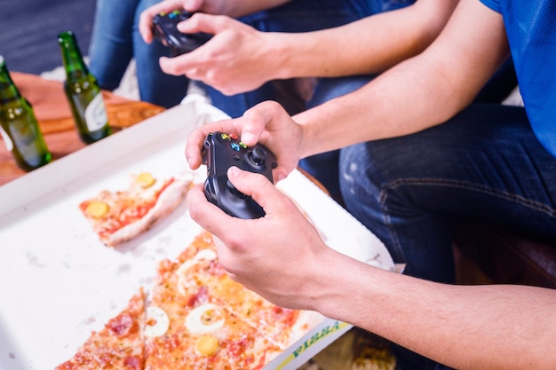 Free photo friends eating pizza and playing on the console