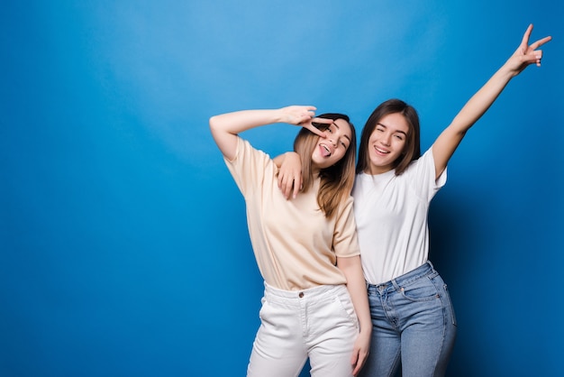 Friends forever. Two cute lovely girl friends in sunglasses posing with smile on blue wall