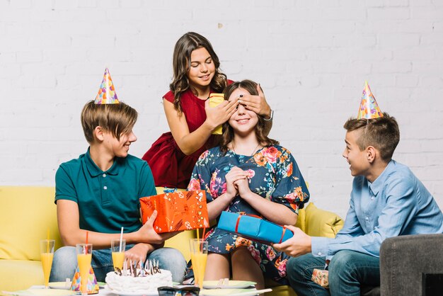 Friends giving gifts to the birthday girl by covering her eyes at party