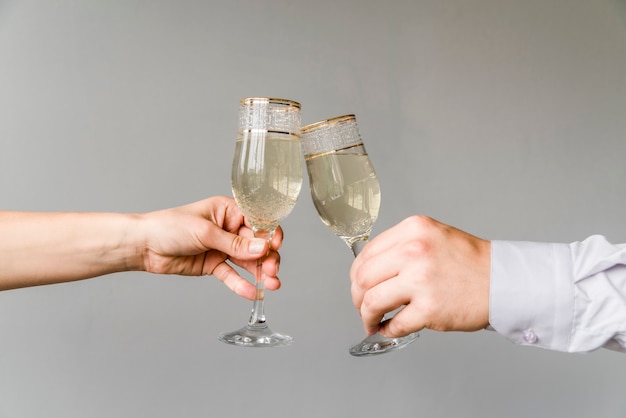 Friends hands clinking glasses of champagne on grey background