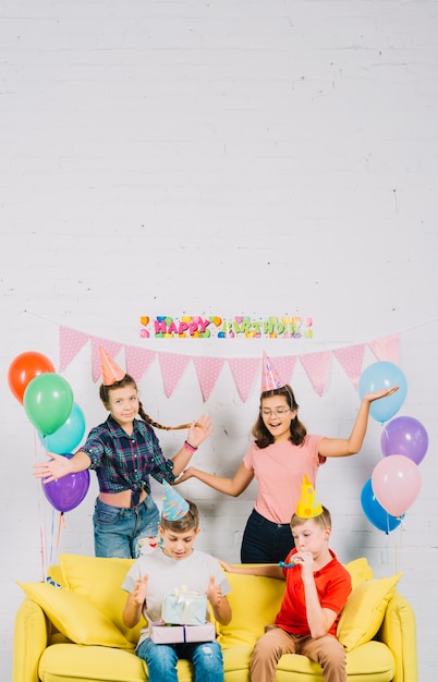 Friends having fun while boy sitting on sofa with birthday gifts