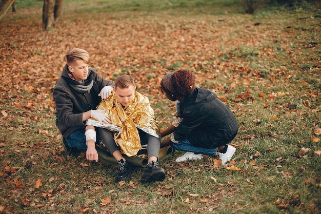 Friends help the guy. The wounded boy sitting on the ground. Providing first aid in the park.