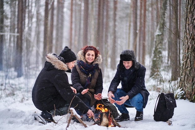 友達は雪に覆われた森でハイキングします。火事で熱くなった若いハイカー。