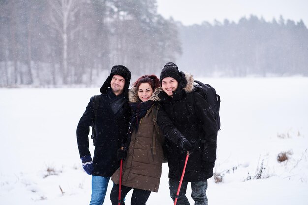 Friends hiking in the cold snowy forest stand in a hug and look at the camera.