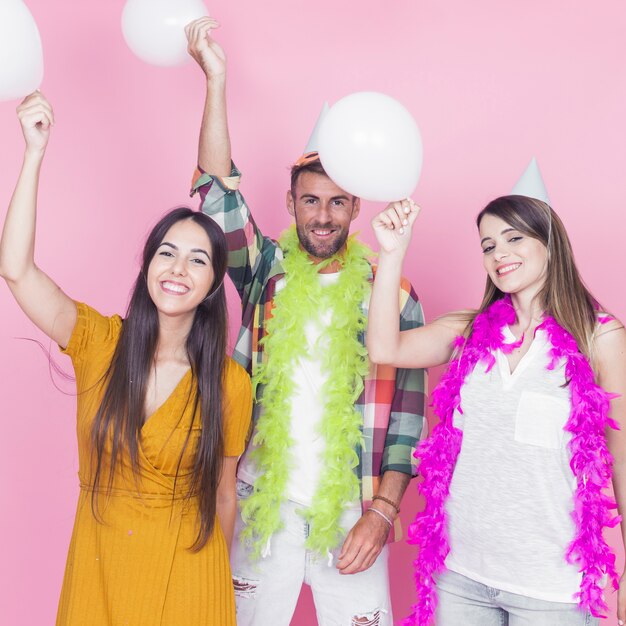 Friends holding white balloons standing against pink background