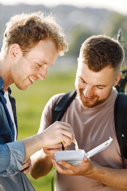 Friends is ready to fishing. Men holding a fishing equipment and looking in a white box with bait for fish. One man wearing rose t-shirt and other blue shirt